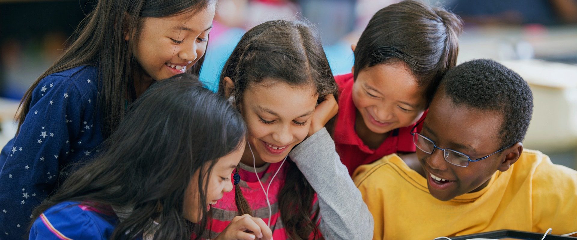 Group of children looking at a tablet laughing together in a classroom.