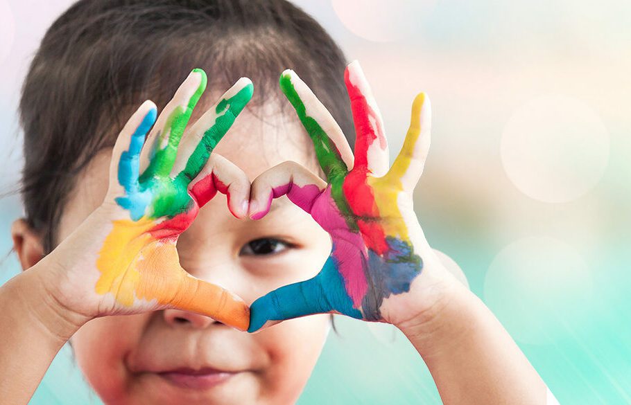 Preschool child making heart with painted hands.